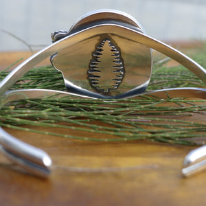 Chunky Nature inspired authentic turquoise cuff bracelet with small flowers on a wood table with pine needles
